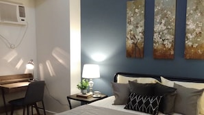 A bedroom with a bed, a desk, and a chair. There are three paintings on the wall. - 1209 Two Residences Marco Polo Cebu (Cebu City)