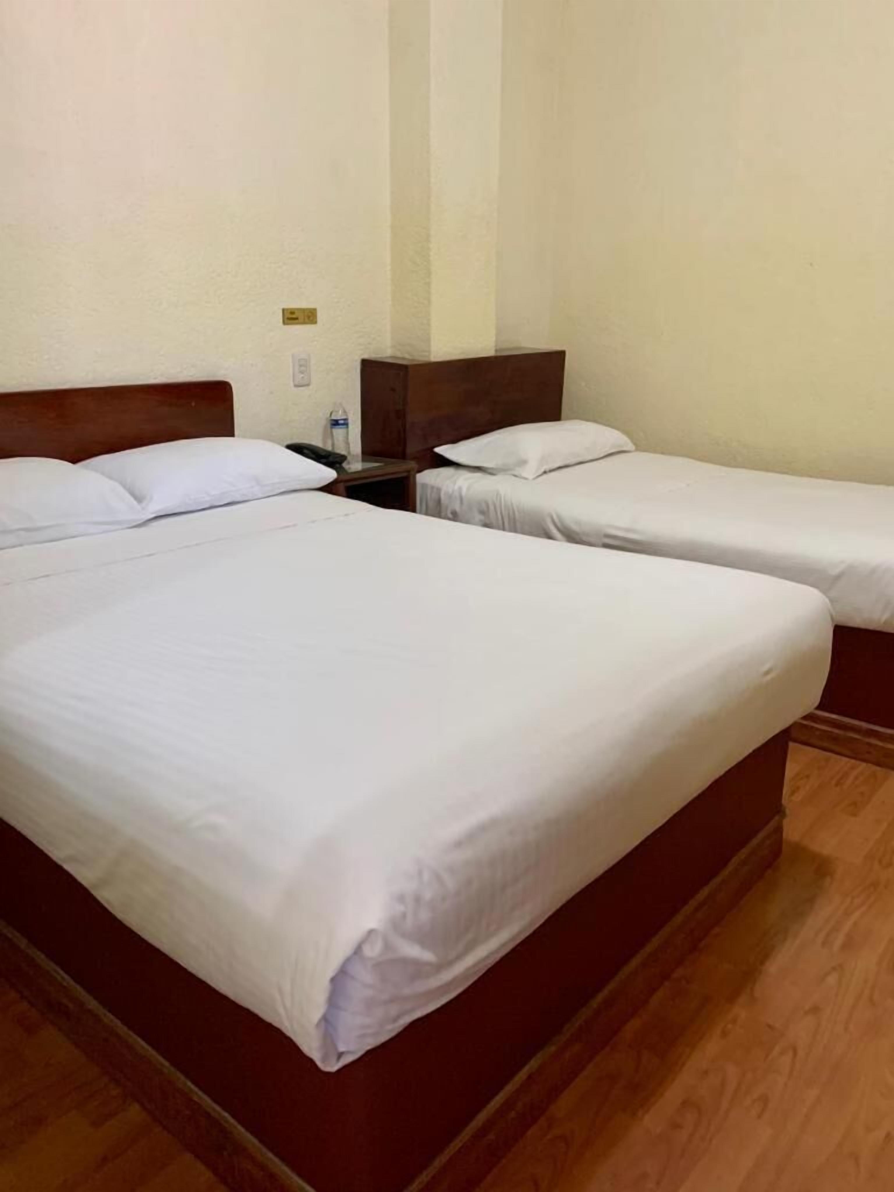 A hotel room with two single beds, a wooden headboard, a nightstand, and a wall socket.