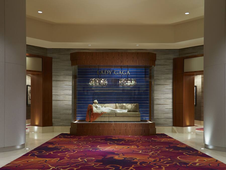 A modern lobby with a central seating area, a decorative wall with 'LADY GAGA' branding, and a patterned carpet.