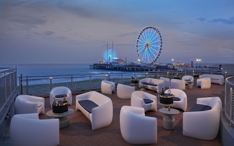 A rooftop bar with white cushioned seating and a large Ferris wheel in the background.