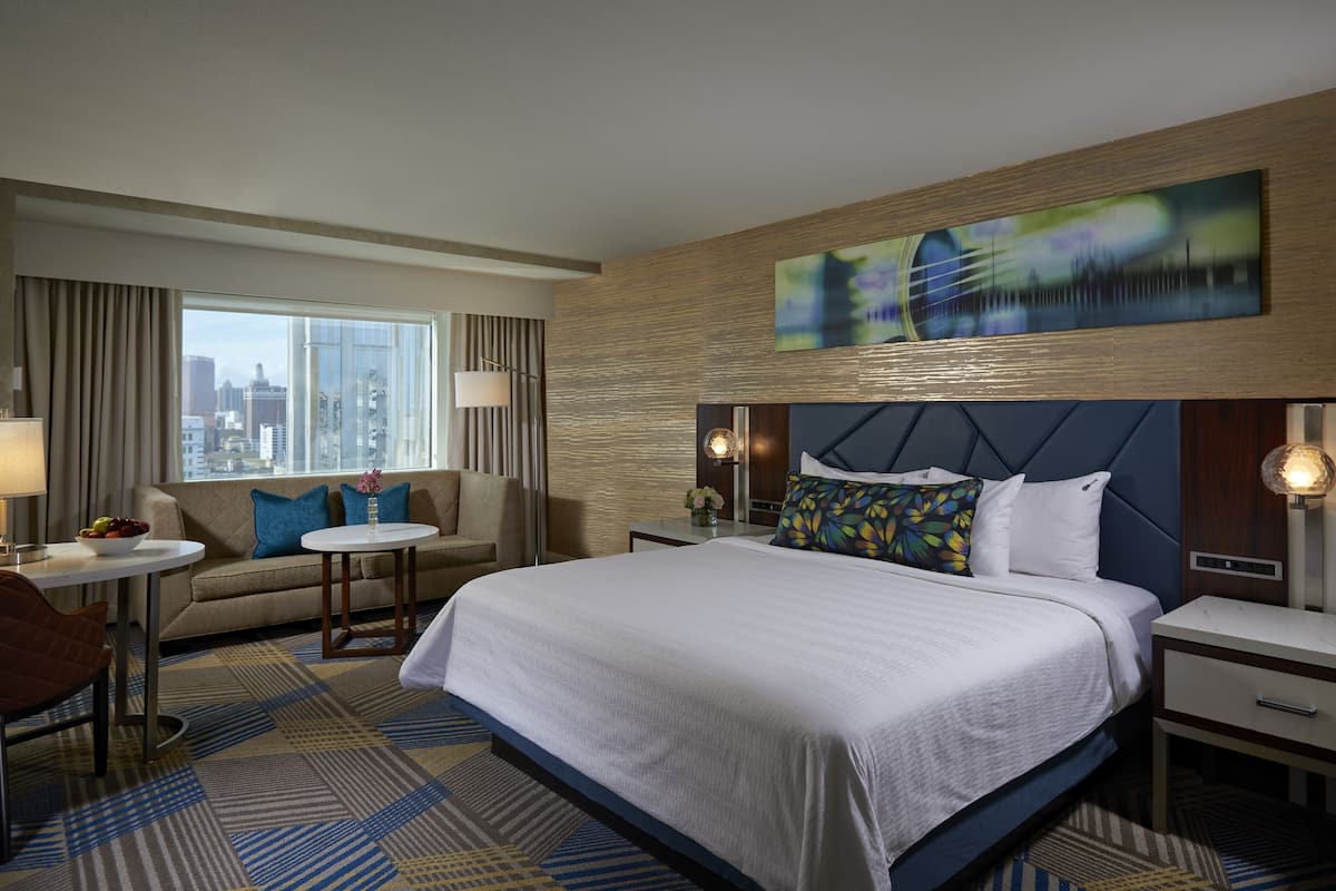 A hotel room with a large bed, a sofa, a small table, and a city view.