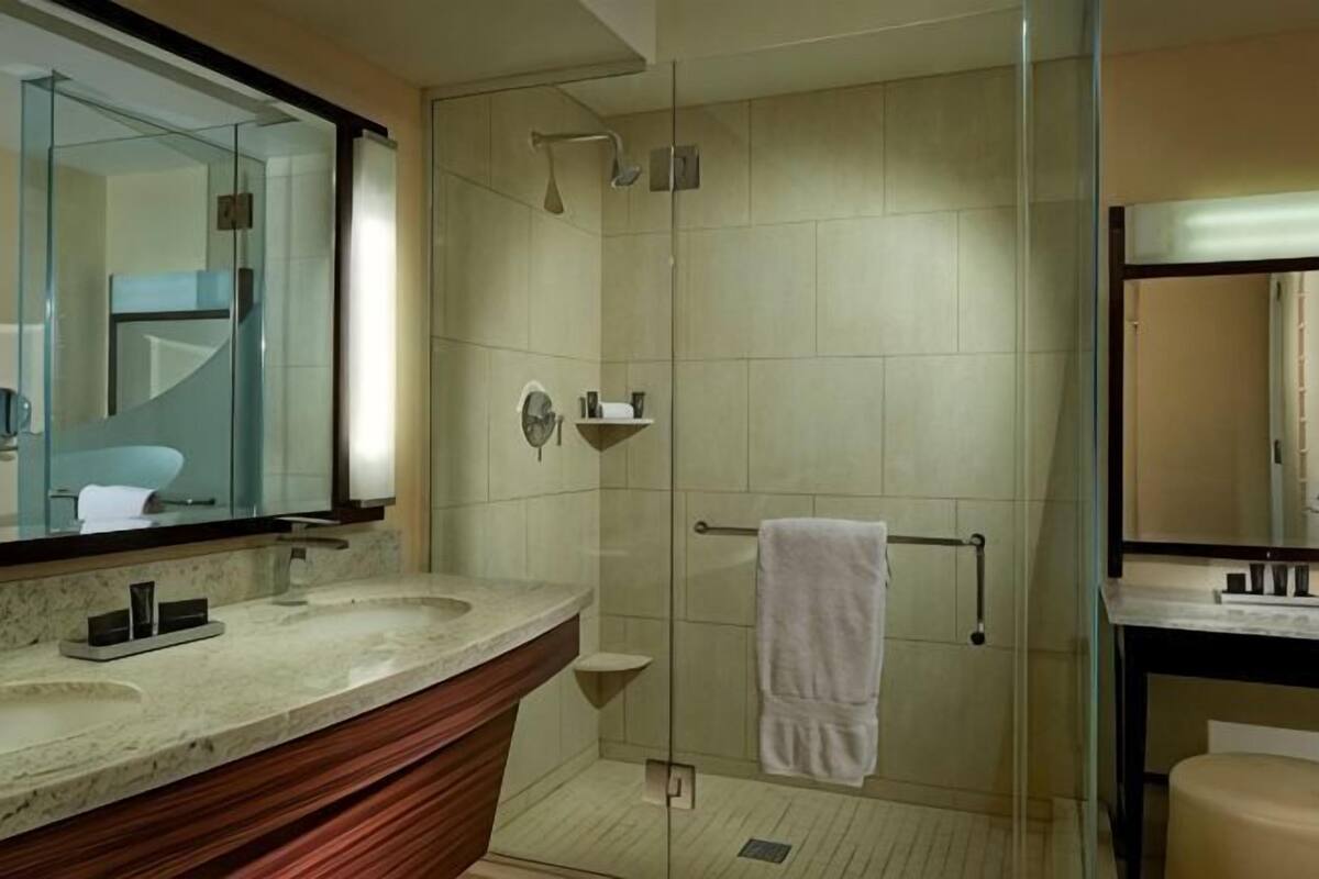 Une salle de bain dotée d’une douche à parois de verre, d’un meuble-lavabo avec un plan de travail en marbre et d’un grand miroir.