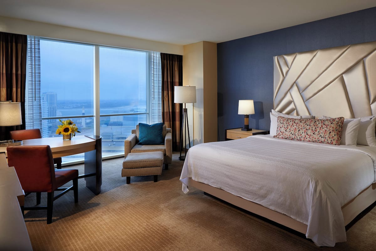 A hotel room with a large bed, a desk, a chair, and a view of the city.