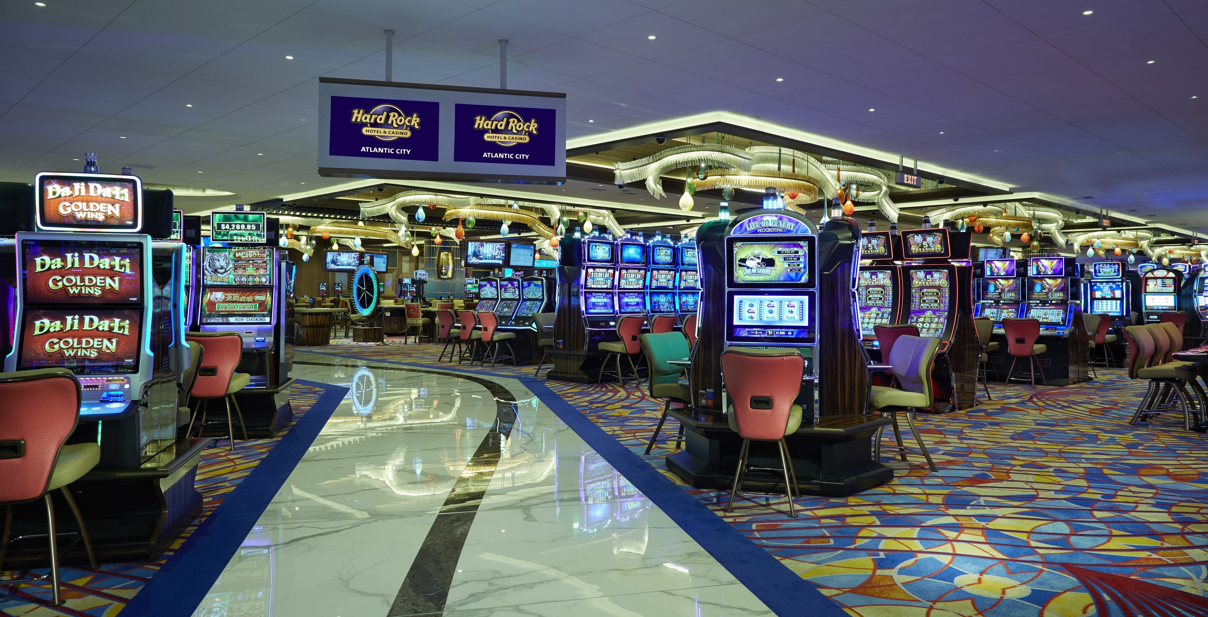 A casino floor with multiple gaming machines, including 'Da Ji Da Li Golden Wins' and 'Hard Rock Casino' signs, and a patterned carpet.