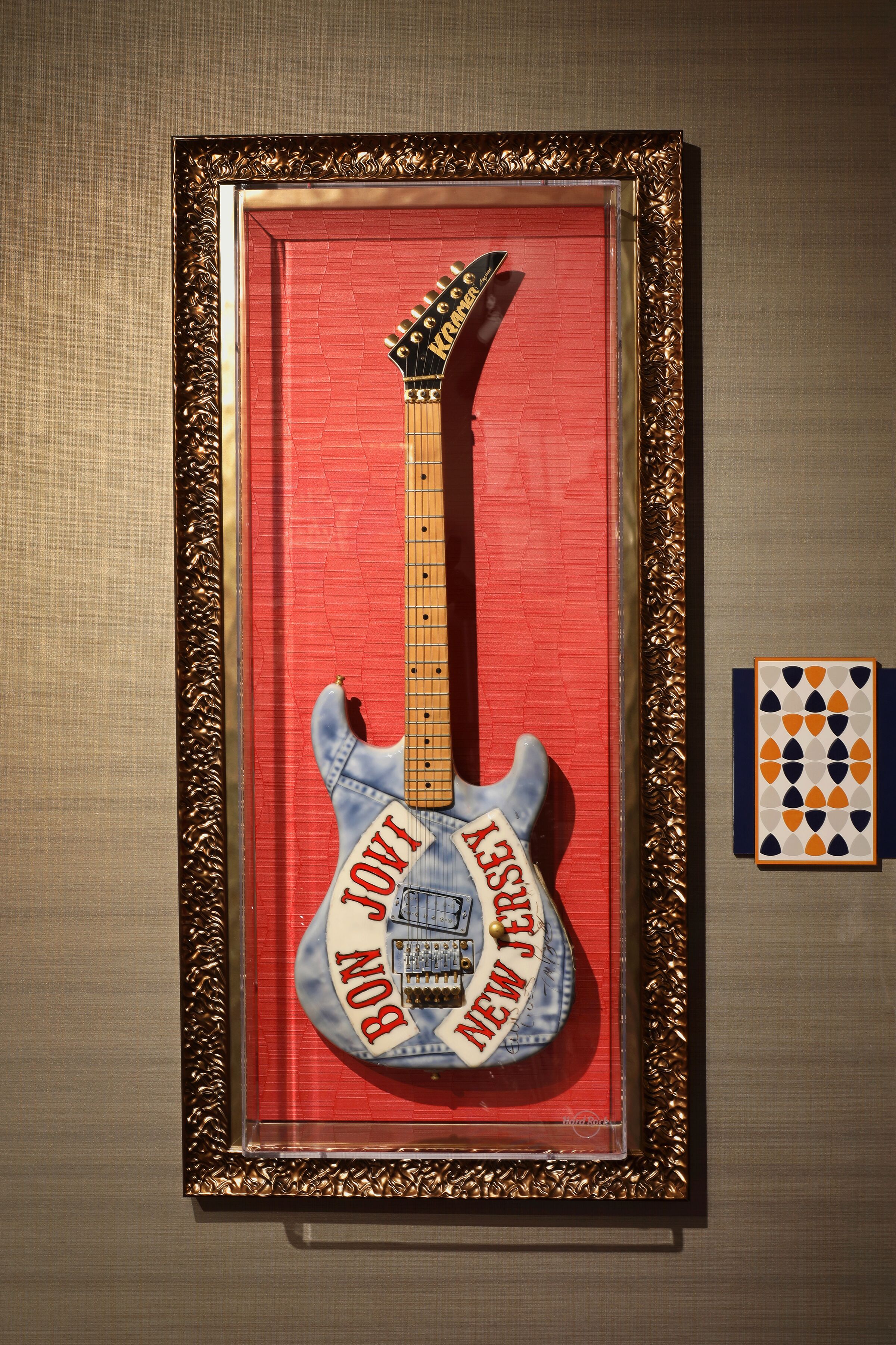 A framed guitar with "JONNY BOWIE" and "NEW JERSEY" on it, placed on a red background.