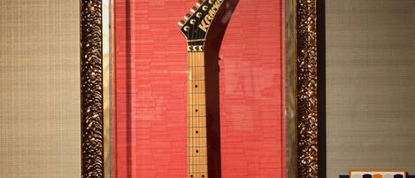 Una guitarra enmarcada con la inscripción "JONNY BOWIE" y "NEW JERSEY" sobre un fondo rojo.
