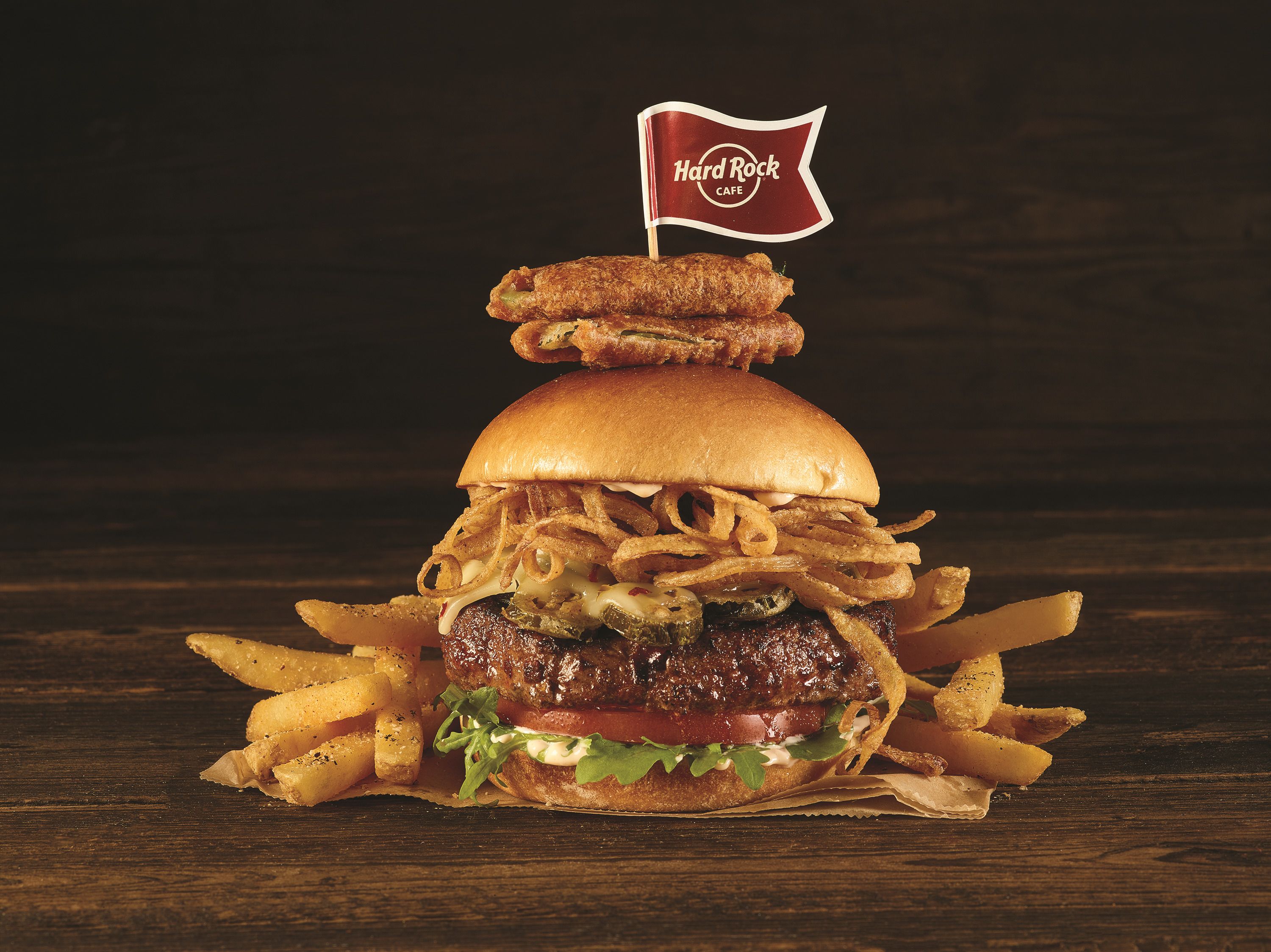 Un hamburger surmonté d’un drapeau, entouré de frites et posé sur une surface en bois.