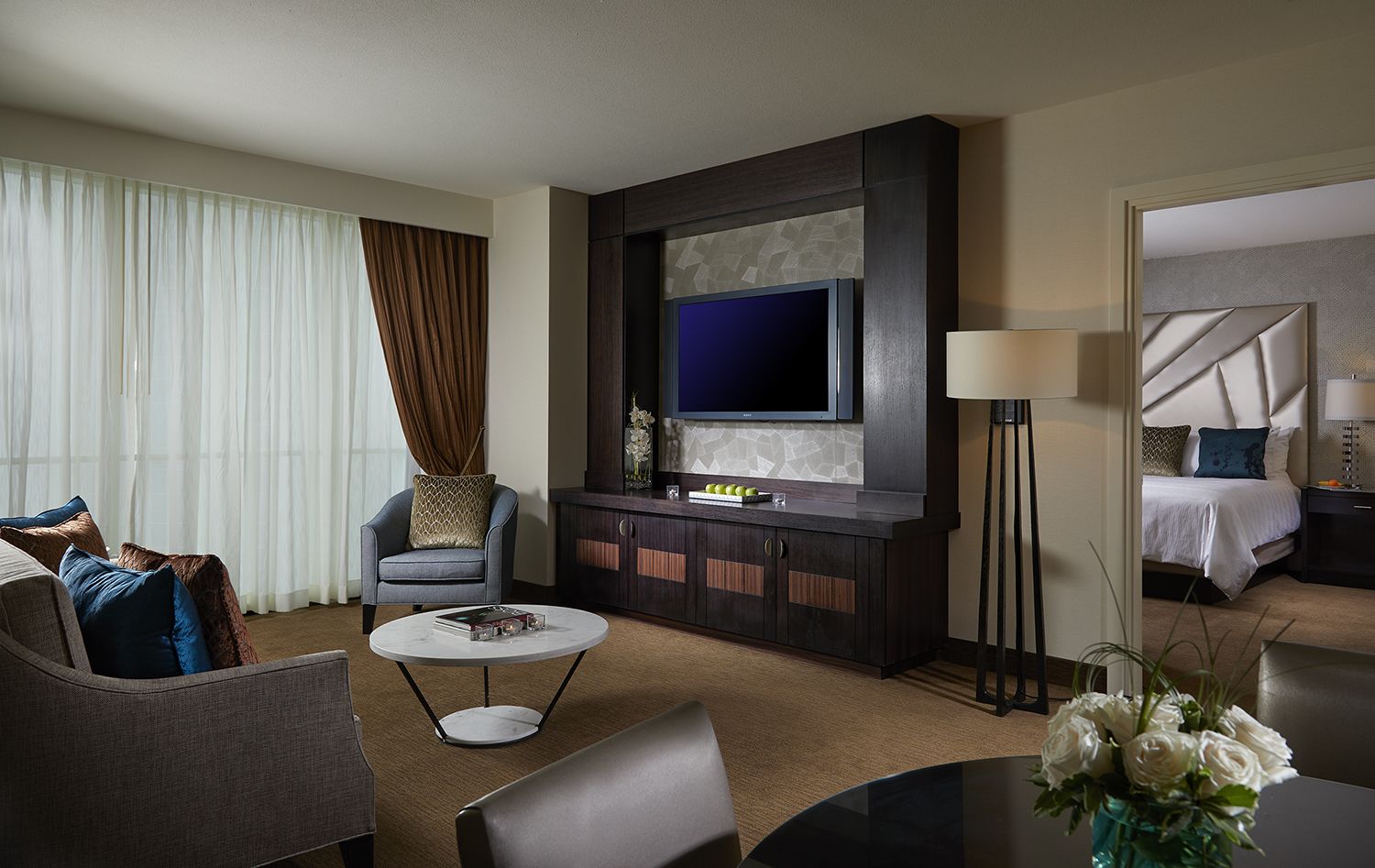 A modern hotel room with a flat-screen TV, a sofa, a coffee table, and a bed with a headboard.