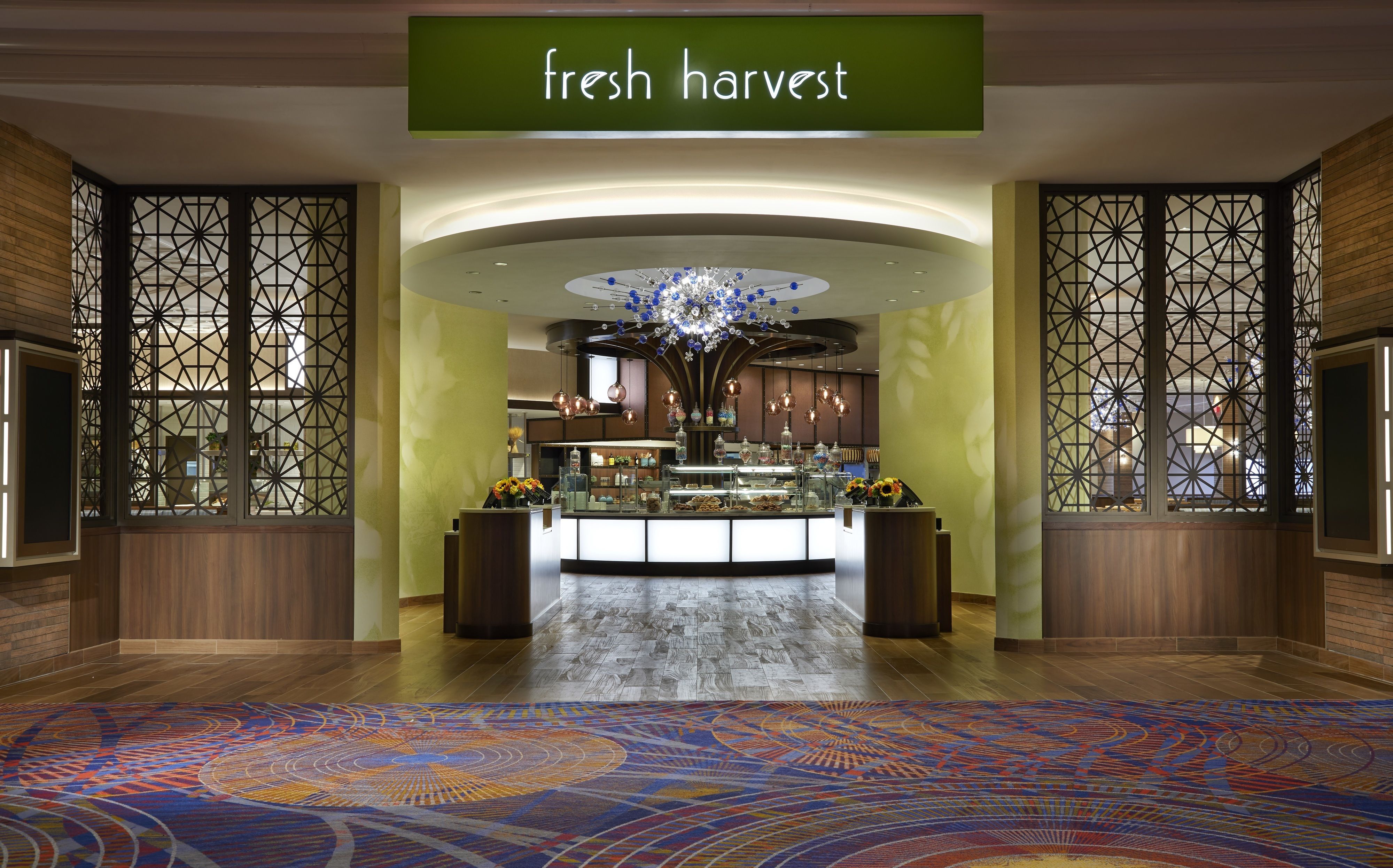 A hotel lobby with a 'fresh harvest' sign, a central chandelier, and a patterned carpet.