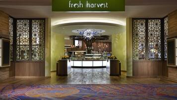 A hotel lobby with a 'fresh harvest' sign, a central chandelier, and a patterned carpet.