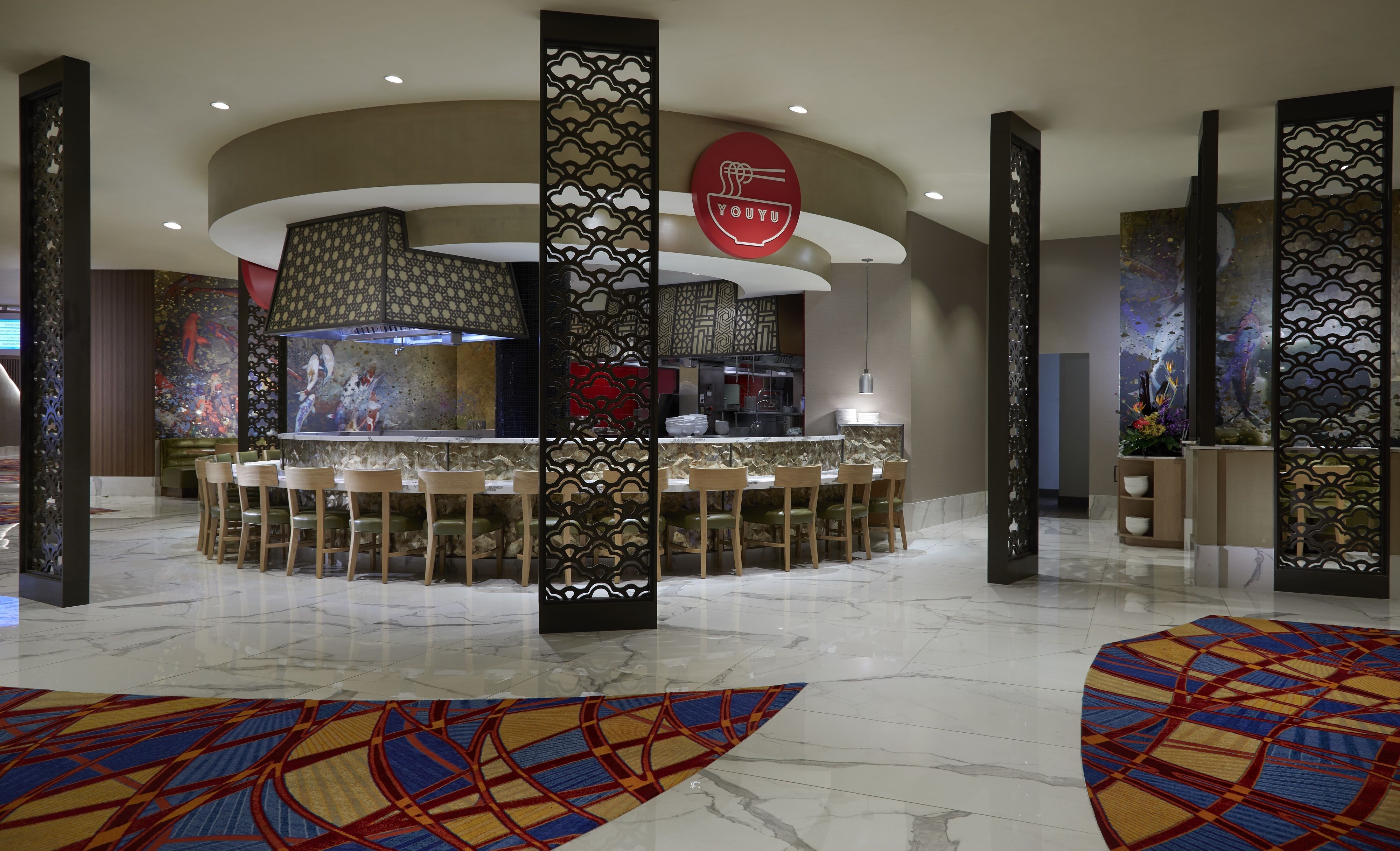 A modern restaurant with a central bar area, seating around the bar, and decorative screens.