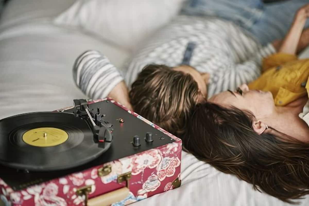 A person lying on a bed with a record player and a floral-patterned box.