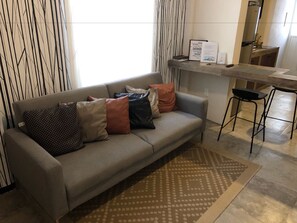 A modern living room with a grey sofa, patterned rug, and a kitchen area with a bar stool.