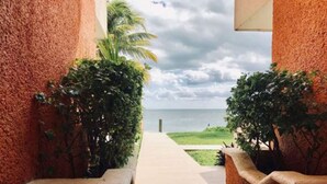 A pathway leading to a beach with a view of the ocean, flanked by red walls and greenery. - Flamingo Beach Plus (Cancun)