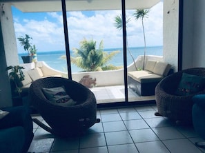 A balcony with two wicker chairs, a sofa, and a potted plant.