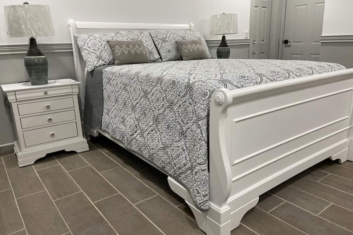 Une chambre à coucher avec un lit blanc, une literie à motifs, une table de chevet avec une lampe et une commode.