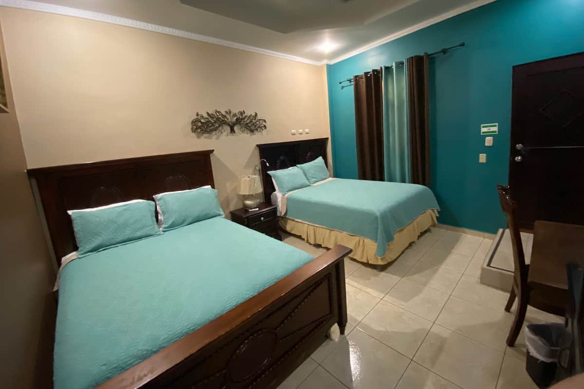 Une chambre d’hôtel avec deux lits, un ventilateur de plafond, un élément décoratif mural et une vue sur l’extérieur par une fenêtre munie de rideaux.