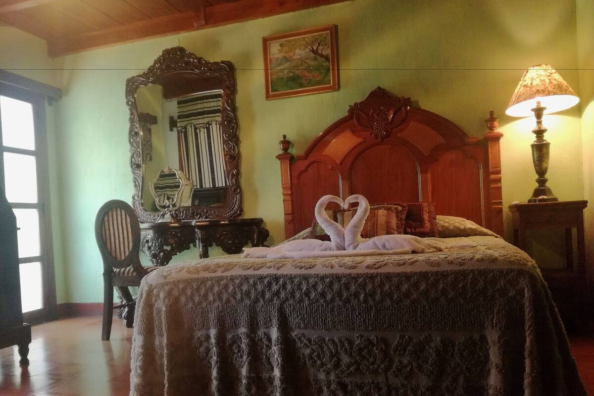 A bedroom with a large bed, a wooden headboard, a mirror, a lamp, and a painting on the wall.