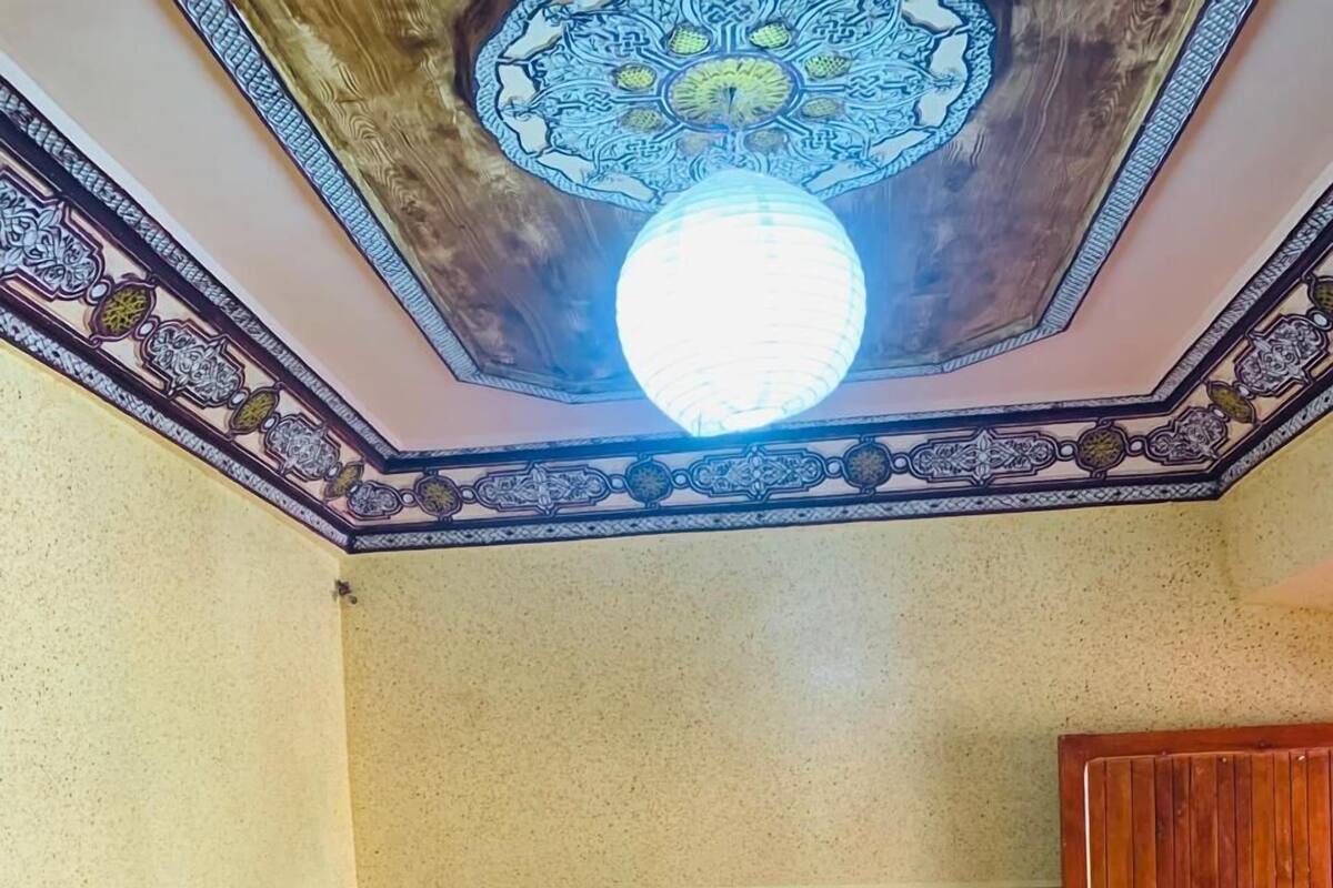 Un dormitorio con cama, almohadas estampadas, un armario de madera y un techo decorativo.