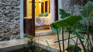 A stone-walled room with a bed, a wooden door, and a small outdoor area with plants. - Verde Morada Hotel Encuentro (Valladolid)