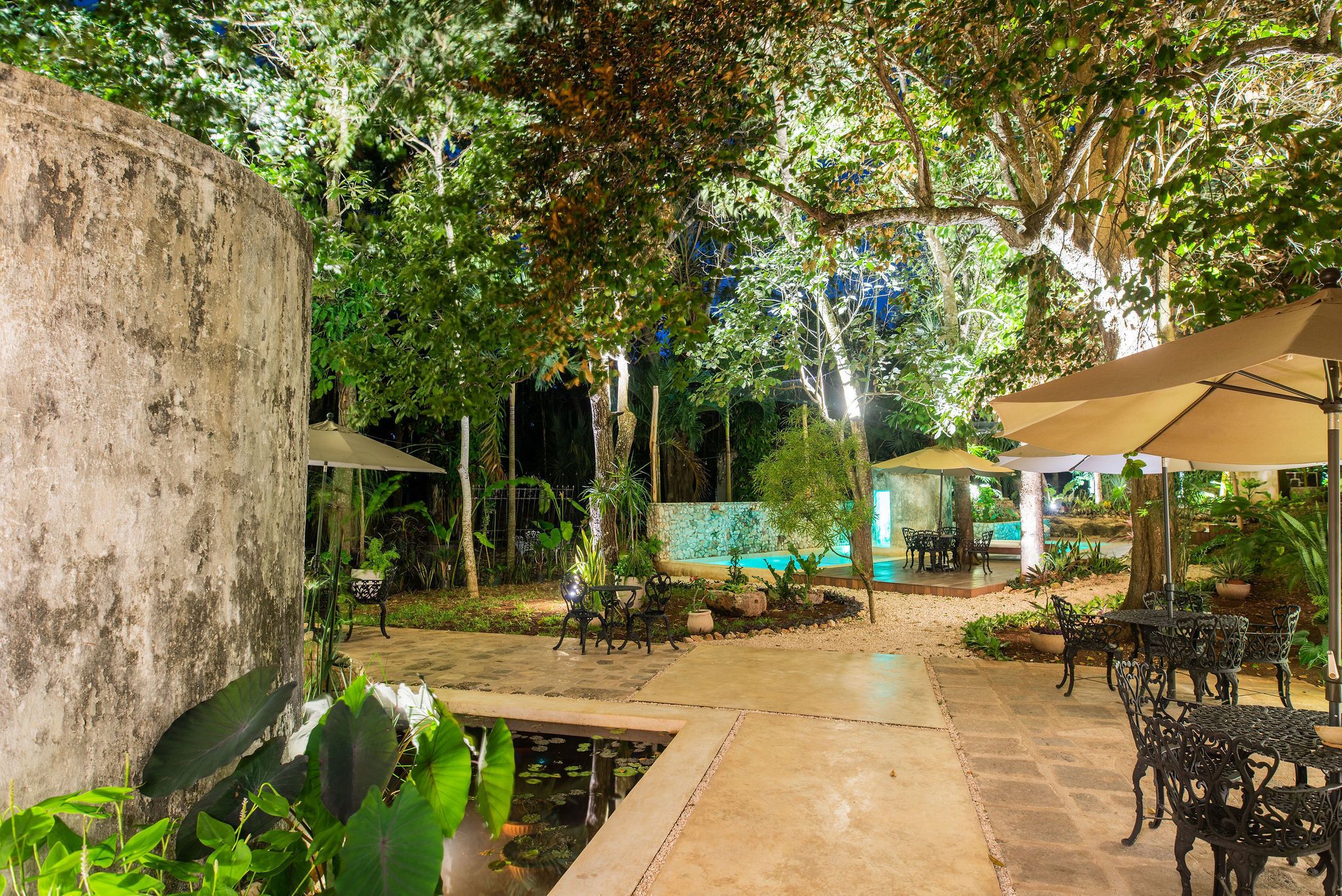 An outdoor patio area with tables and chairs, surrounded by lush greenery and a small pond.