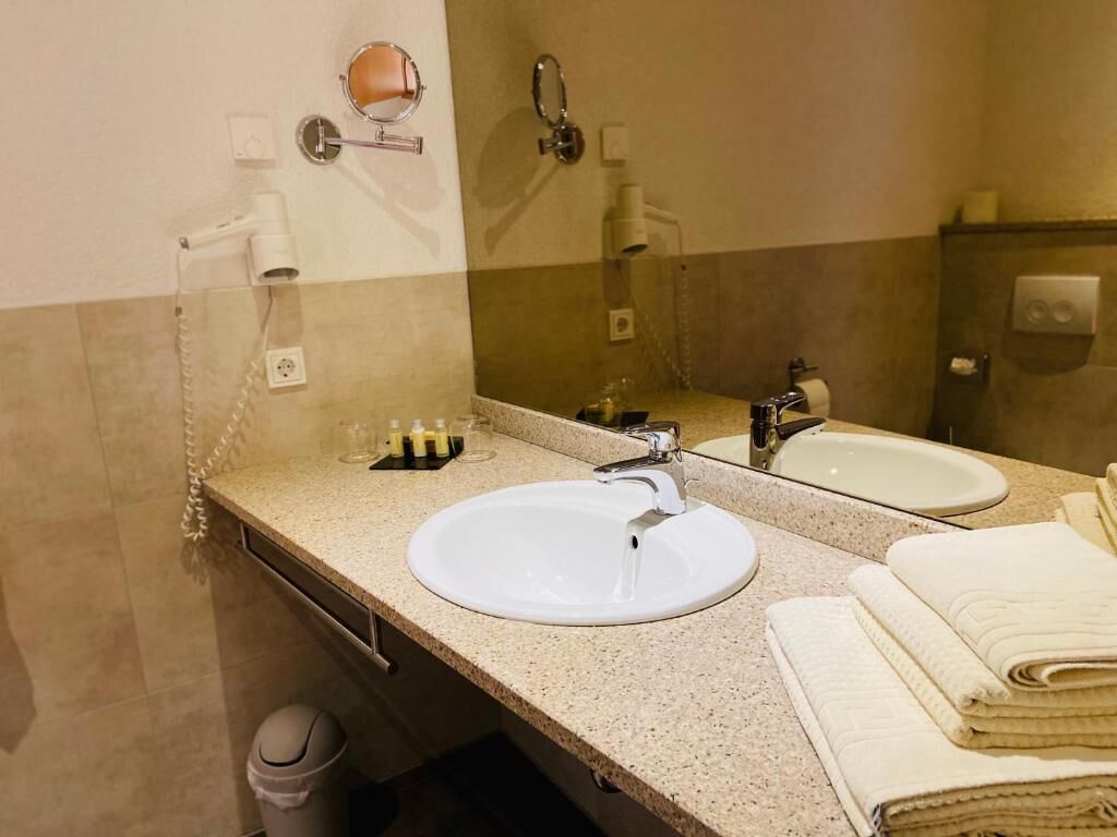 A bathroom with two sinks, a mirror, a hairdryer, and a trash bin.