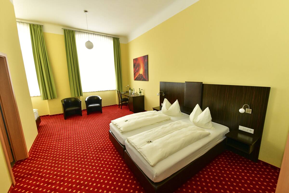 A hotel room with two beds, a desk, a chair, and a window with curtains.