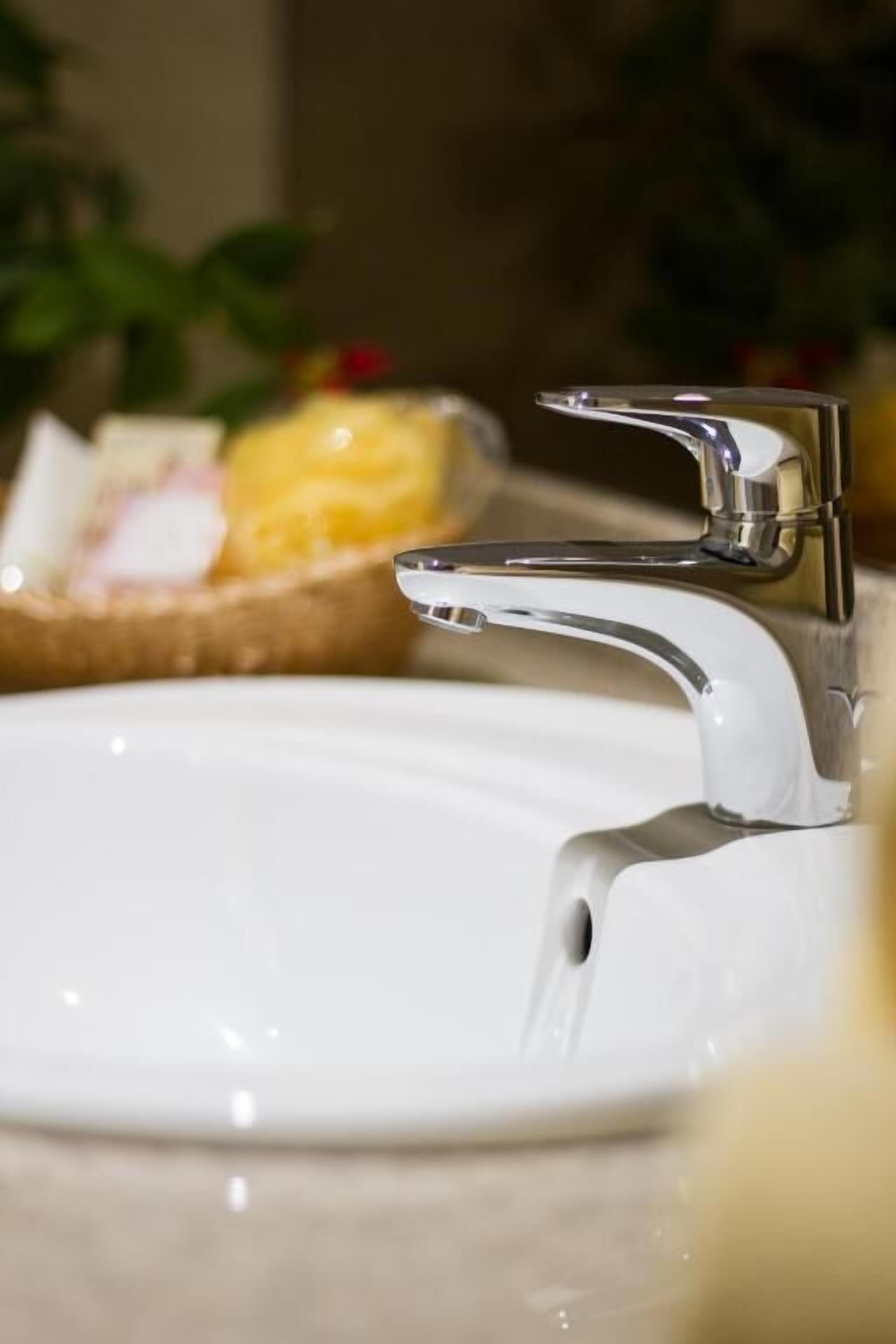 Un lavamanos moderno con grifo cromado, un lavabo blanco y una cesta de artículos de aseo en el fondo.