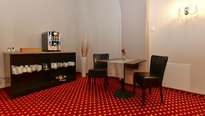 A dining area with a red patterned carpet, a table with chairs, a bookshelf, and a wall-mounted light fixture. - Pension Katharinenschule (Eisenach)