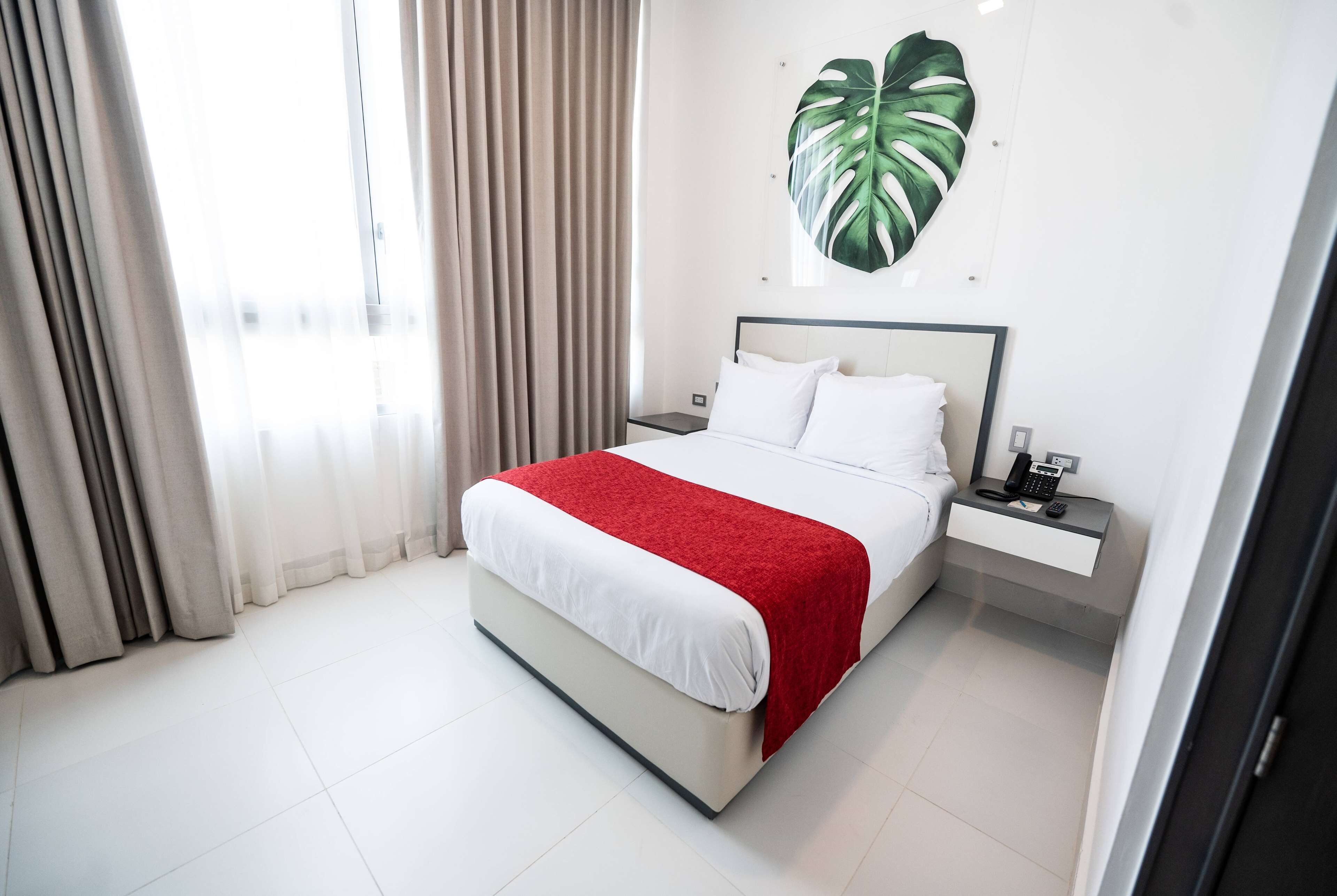 A hotel room with a bed, a nightstand, a phone, and a large plant on the wall.