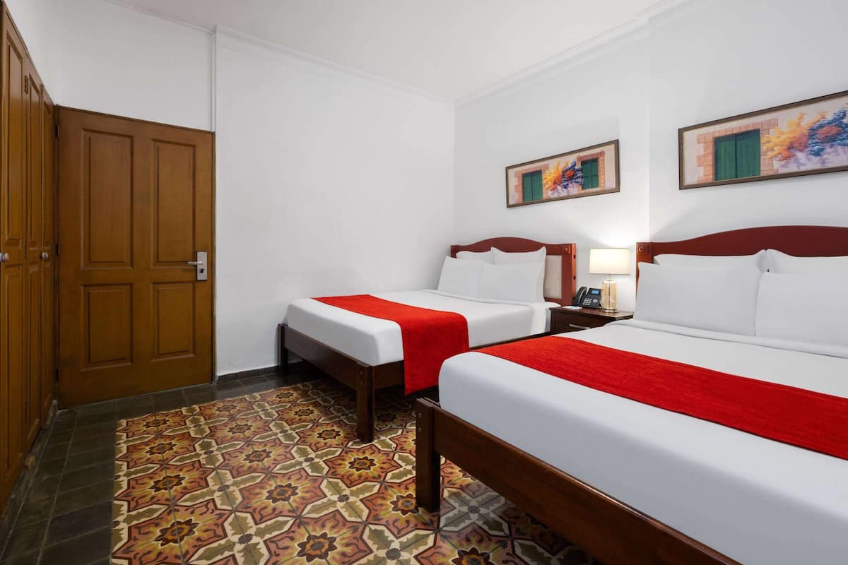 A hotel room with two beds, a wooden wardrobe, a patterned floor, and a painting on the wall.