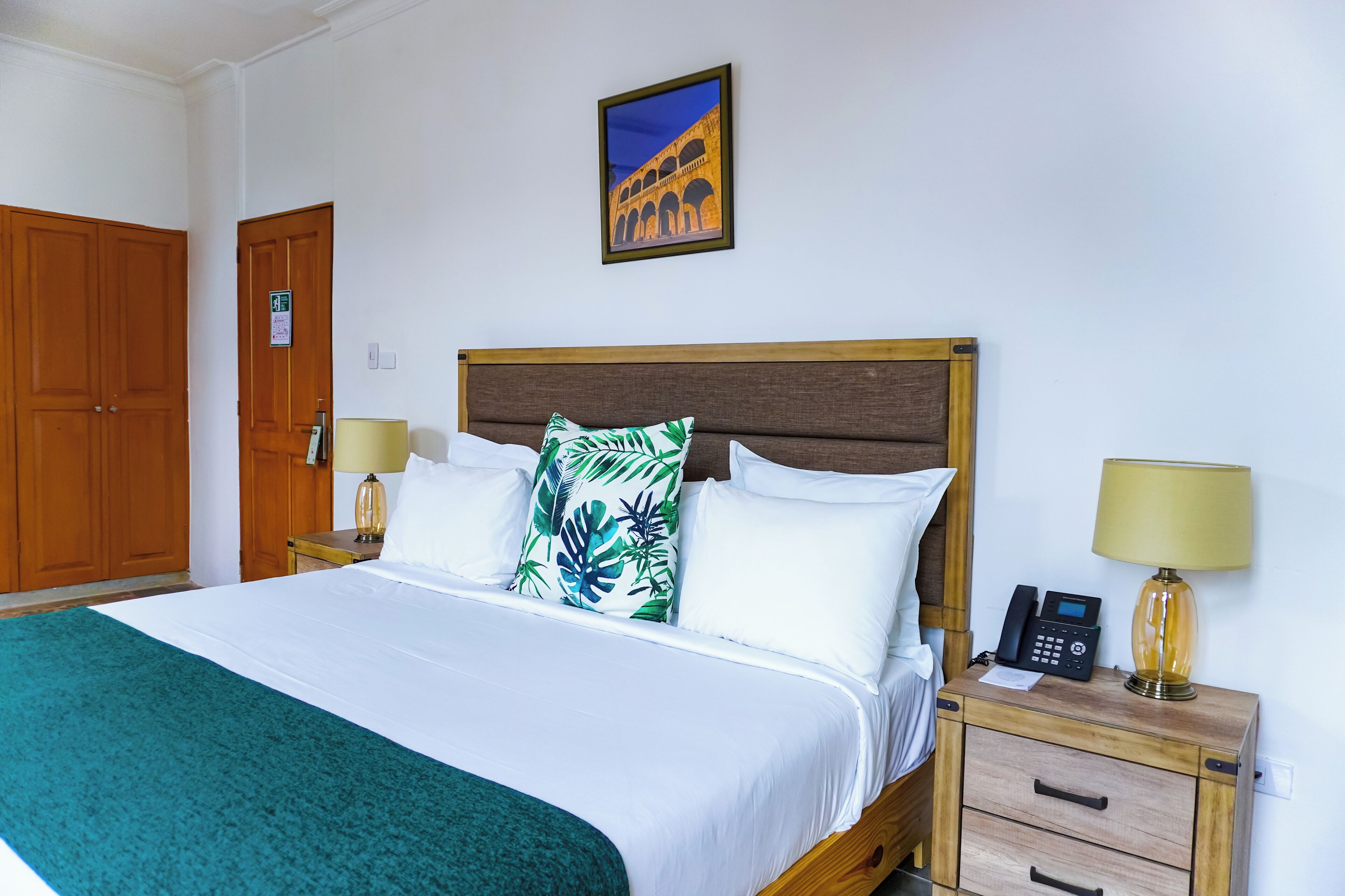A neatly made bed with white linens and a green throw, a wooden headboard, and two bedside tables with lamps and a phone.