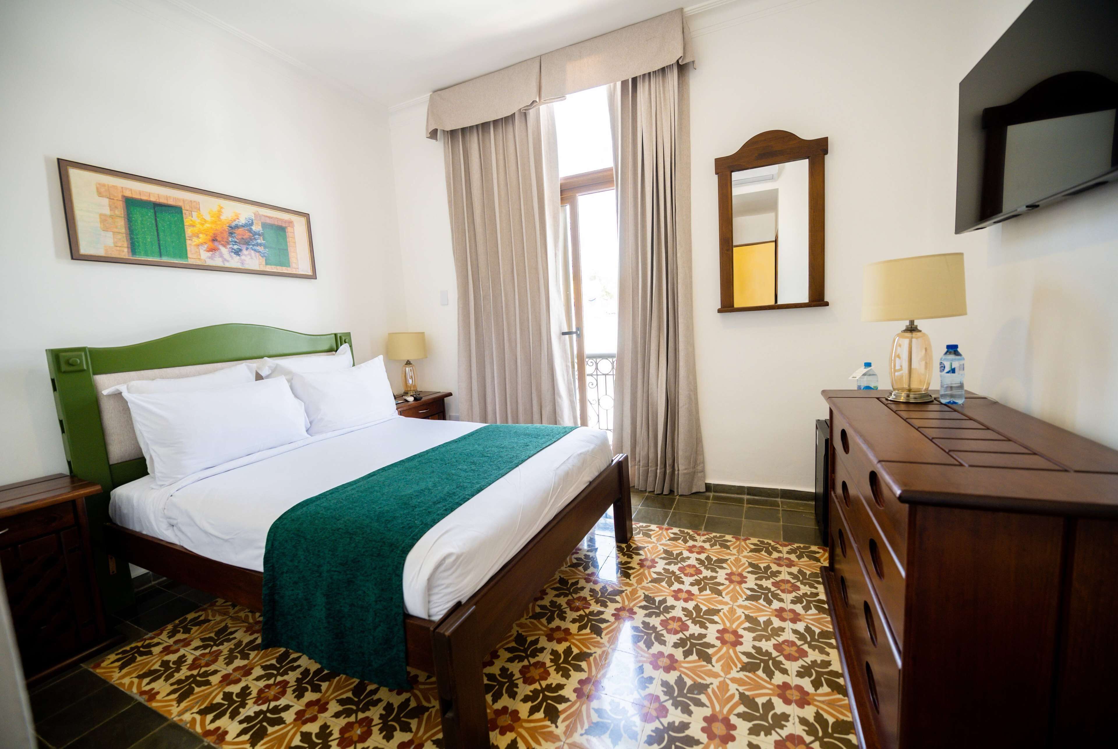 A hotel room with a bed, a dresser, a TV, and a window with curtains.
