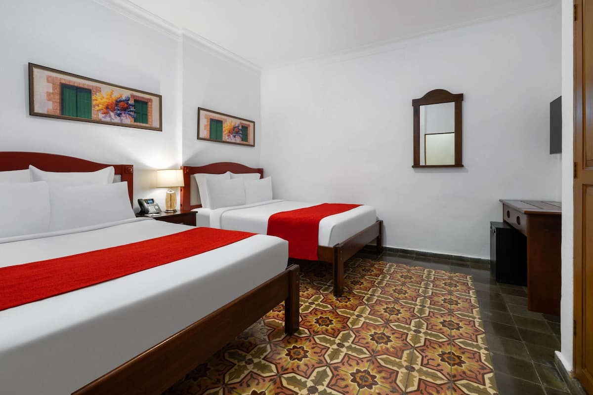 A hotel room with two beds, a small desk, a telephone, and a mirror.
