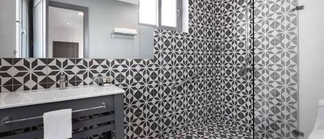 Un baño moderno con un estampado geométrico de azulejos, cabina de ducha de vidrio y tocador con perchero.