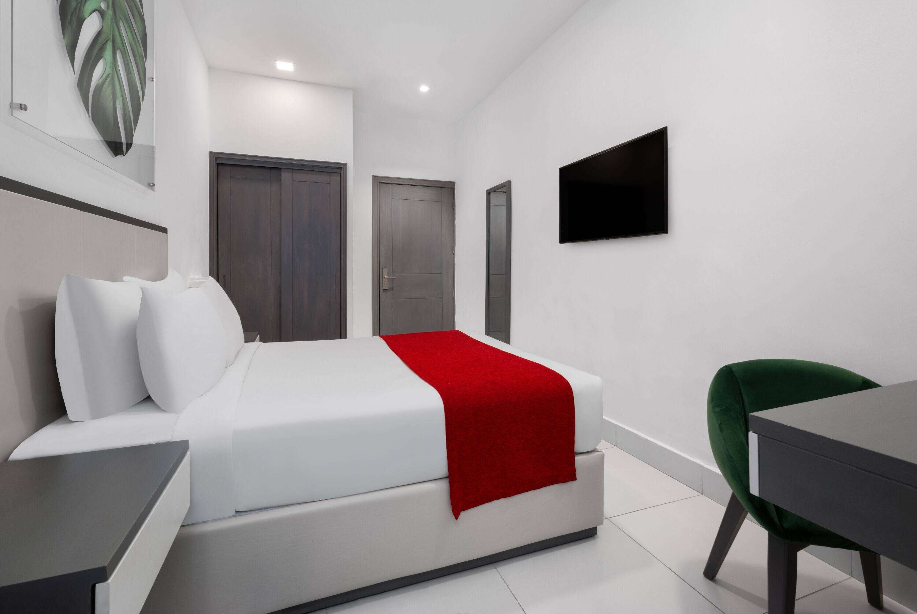 Ein modernes Hotelzimmer mit einem Bett, einem Schreibtisch, einem grünen Sessel und einem an der Wand befestigten Fernseher.