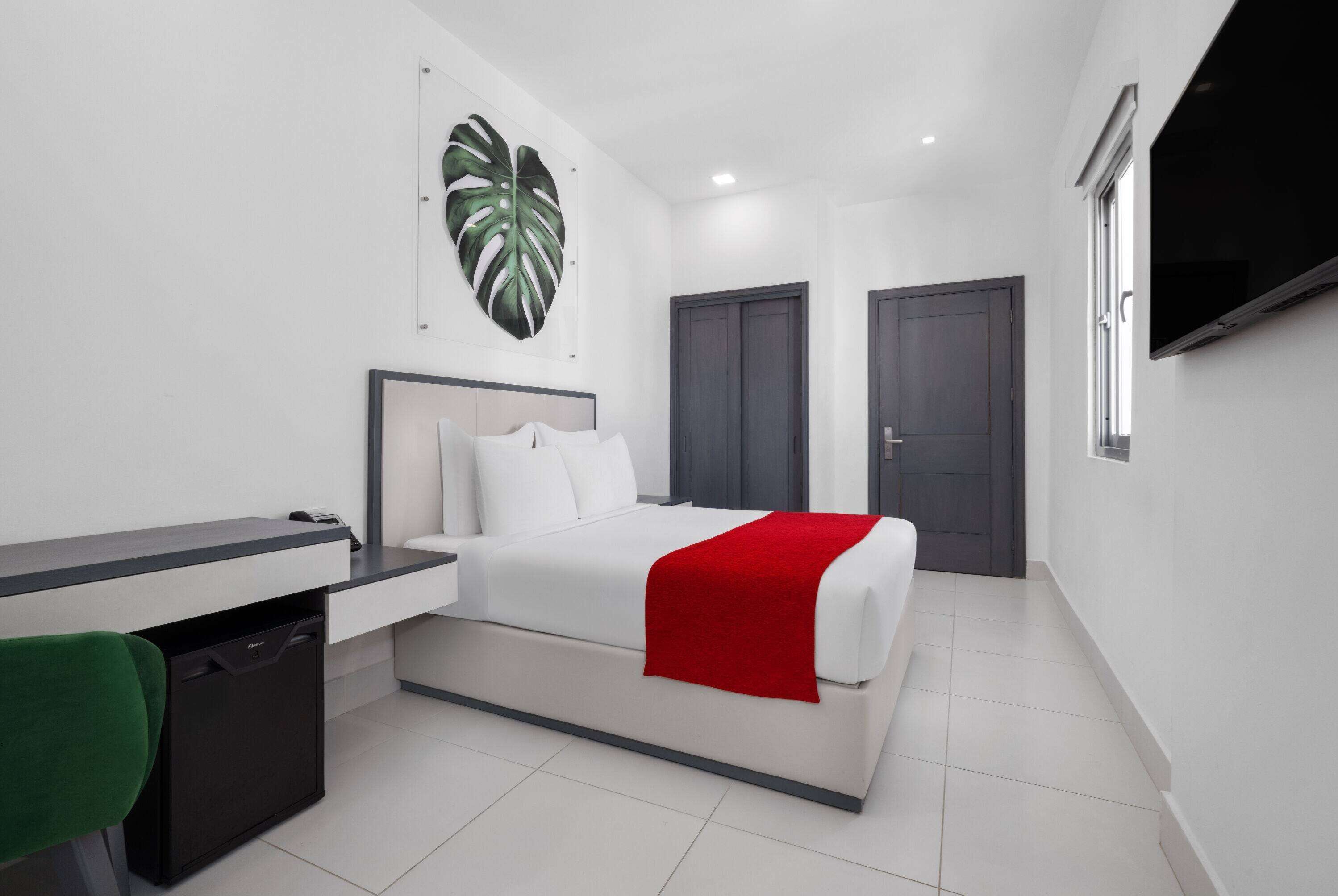 A modern hotel room with a bed, a desk, a chair, a TV, and a large window.