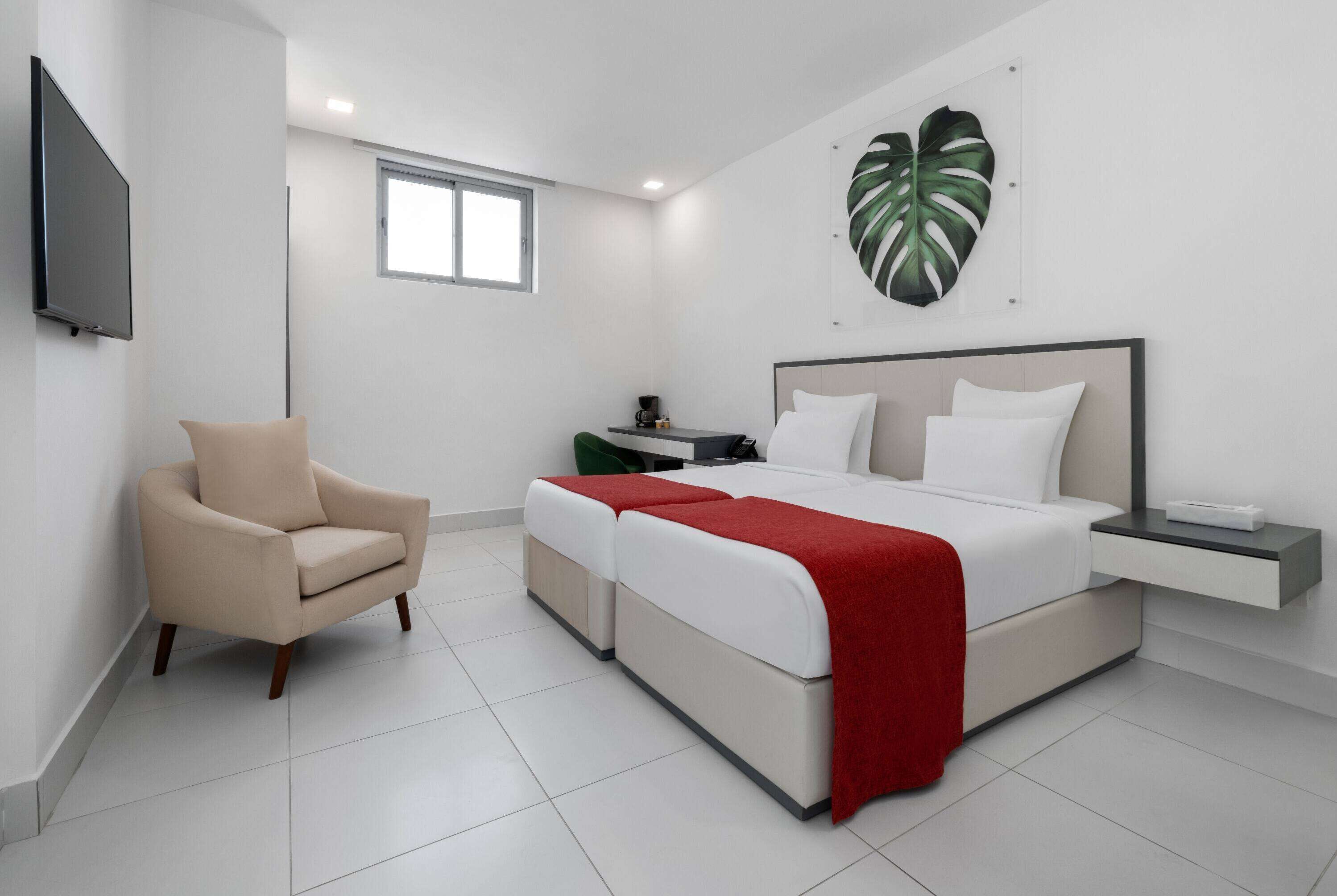 A modern bedroom with a bed, bedside tables, a chair, and a large plant.