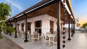 An outdoor cafe area with white tables and chairs, a wooden pergola, and hanging pendant lights. - Gran Hotel Europa Santo Domingo, Trademark by Wyndham (Santo Domingo)