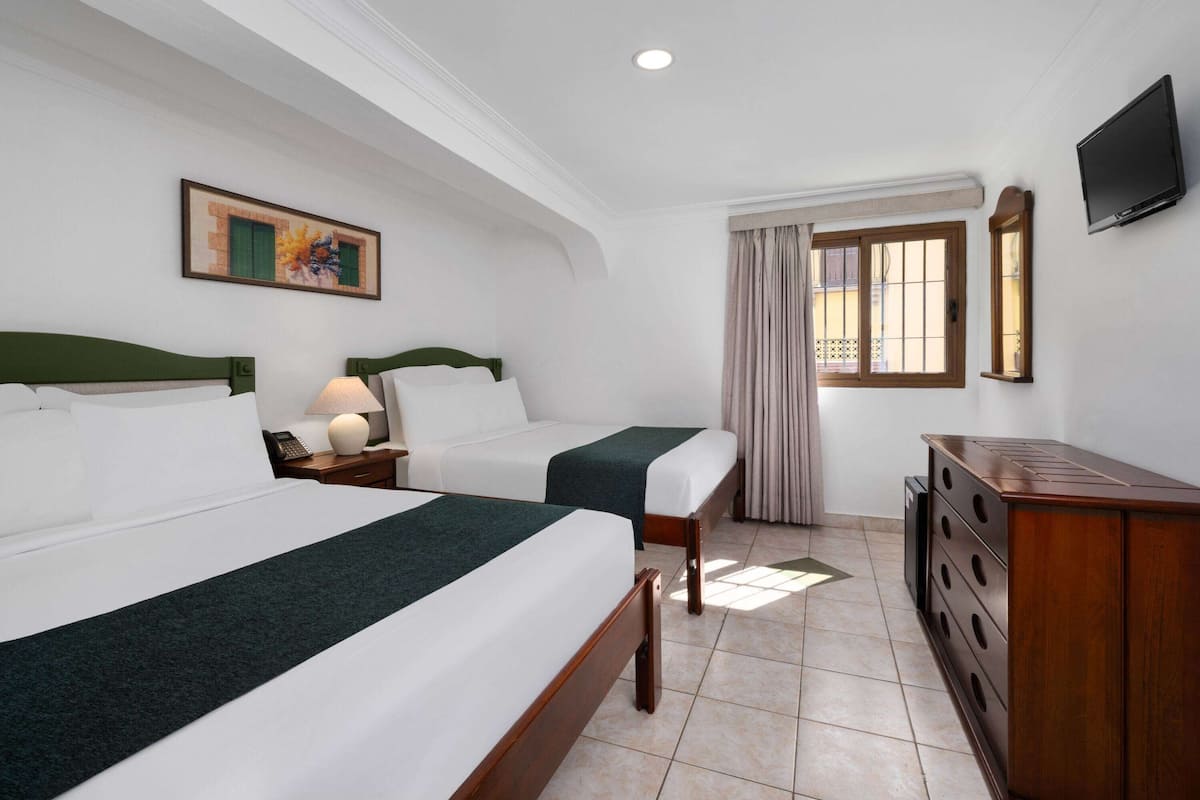 A hotel room with two beds, a desk, a television, and a window with curtains.