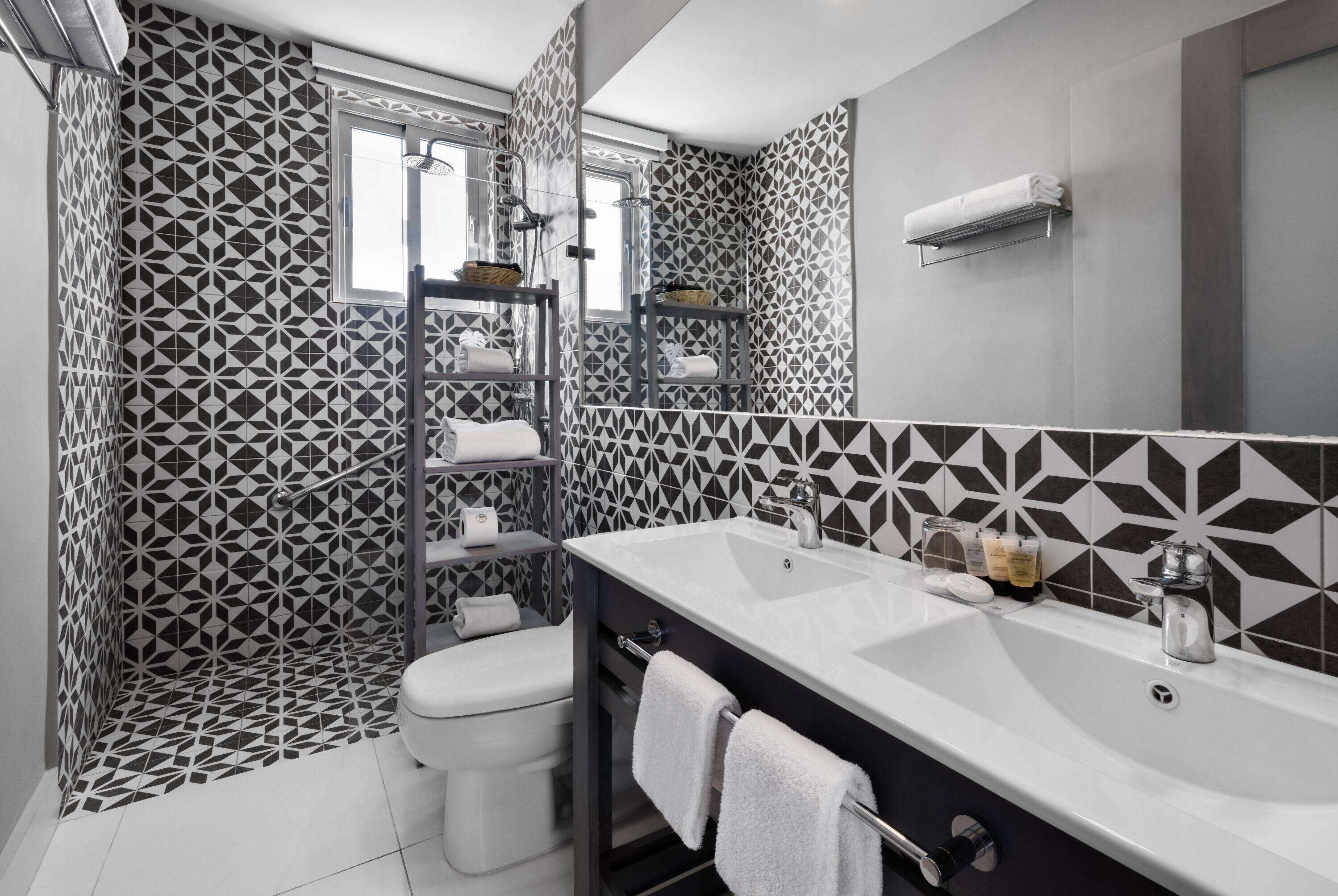Uma casa de banho moderna com um painel de azulejos geométrico, uma pia branca com espelho e zona de duche.