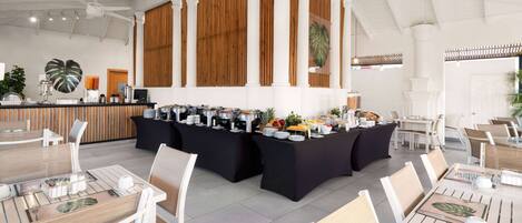Un comedor moderno con techos altos, columnas blancas y una mesa buffet central.