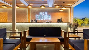 A modern lounge area with a wooden bench, tables, and hanging lights. A neon sign reads "SKY EUROPA". - Gran Hotel Europa Santo Domingo, Trademark by Wyndham (Santo Domingo)