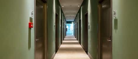 A long, narrow hallway with doors on both sides, leading to a bright room at the end.
