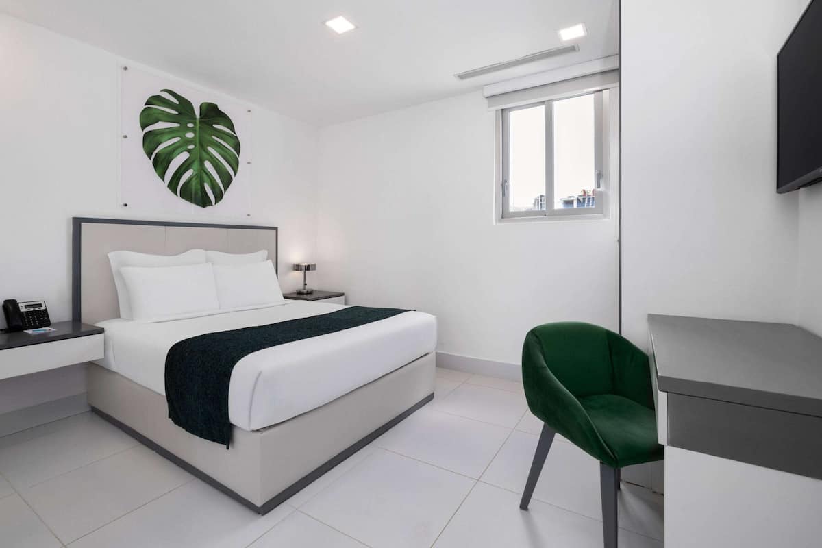 A modern bedroom with a bed, bedside table, green chair, and a large window.