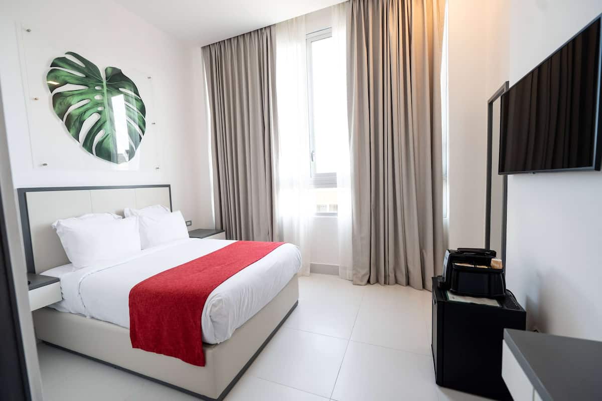 A hotel room with a bed, a large wall art piece, a flat-screen TV, and a window with curtains.