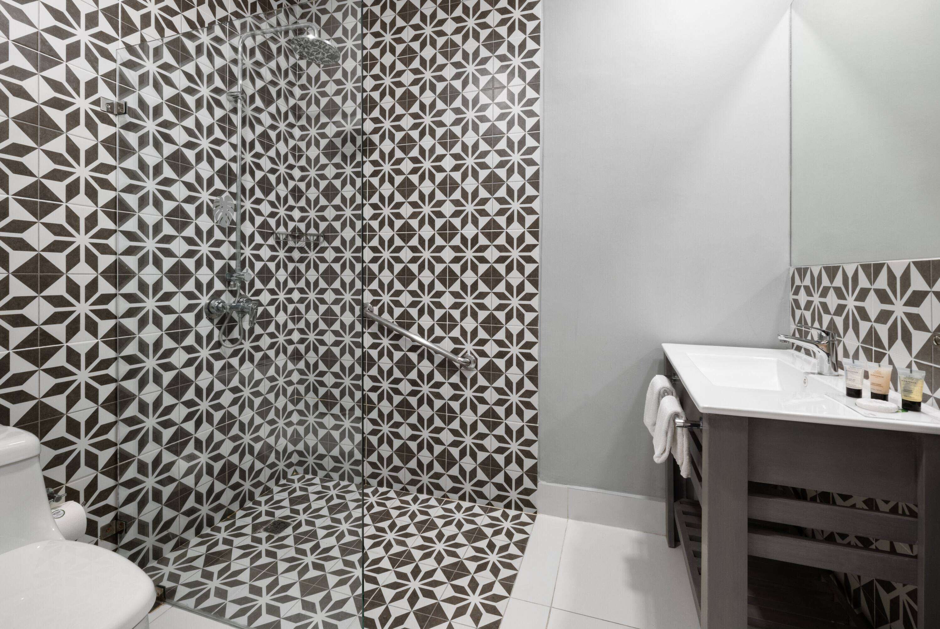 Une salle de bain avec un mur de douche orné d’un motif géométrique, un lavabo blanc et des toilettes.