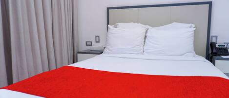 A neatly made bed with white and red bedding, a bedside phone, and a wall-mounted light fixture.
