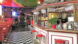 En bar med gulv i skakmønster, røde barstole og en neonskilte.