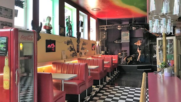 En diner med røde bænke, gulv i skakmønster og en scene til live musik.